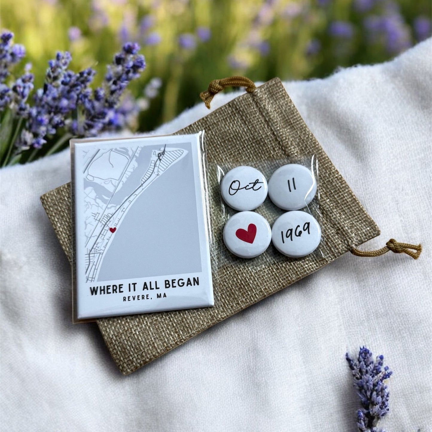 Set of buttons with a card and burlap pouch on a white surface with lavender flowers.