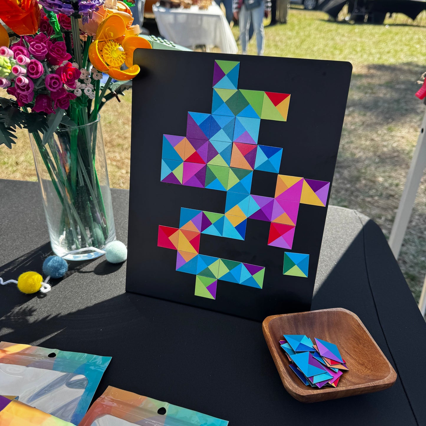 Another angle of a display of magnetic mosaic tiles at a vendor market with a magnet board and pieces for customers to test, and packaged tiles on the table in colorful pouches