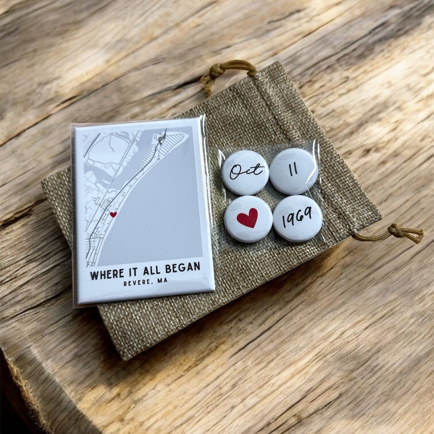 Set of three small white stones with red hearts and numbers, placed on a textured fabric pouch with a map and text on a wooden surface.