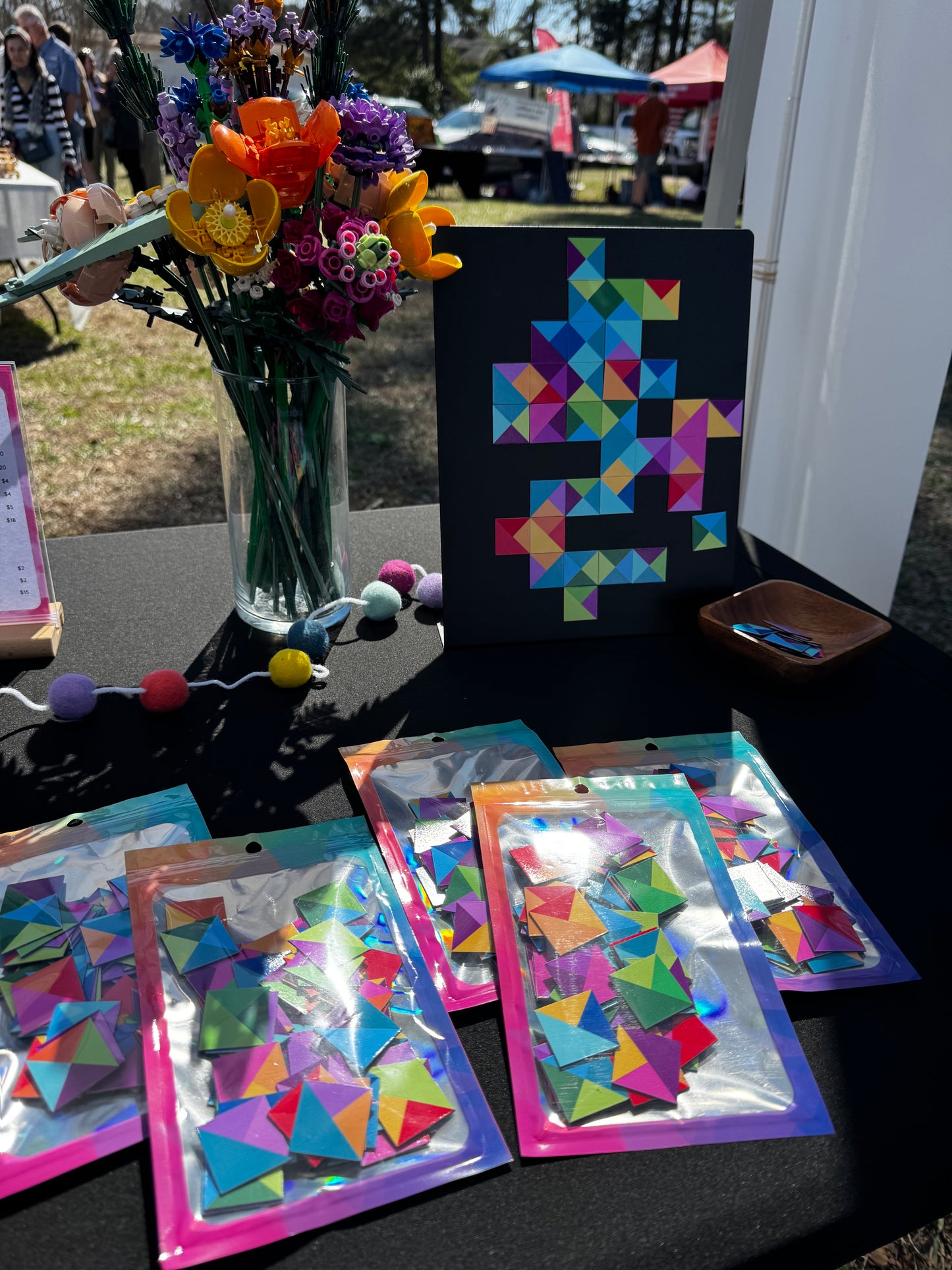 Display of magnetic mosaic tiles at a vendor market with a magnet board and pieces for customers to test, and packaged tiles on the table in colorful pouches