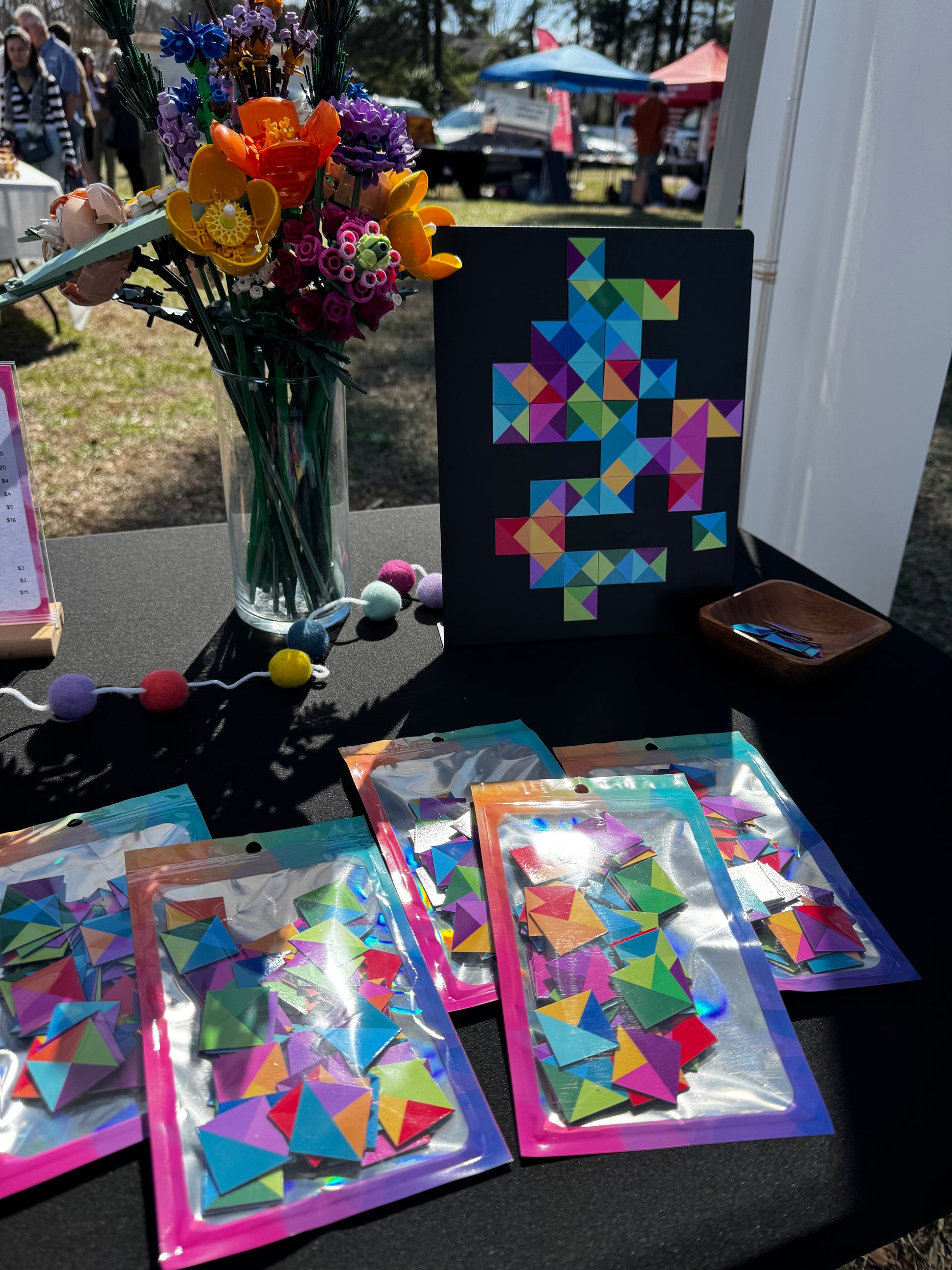 Display of magnetic mosaic tiles at a vendor market with a magnet board and pieces for customers to test, and packaged tiles on the table in colorful pouches